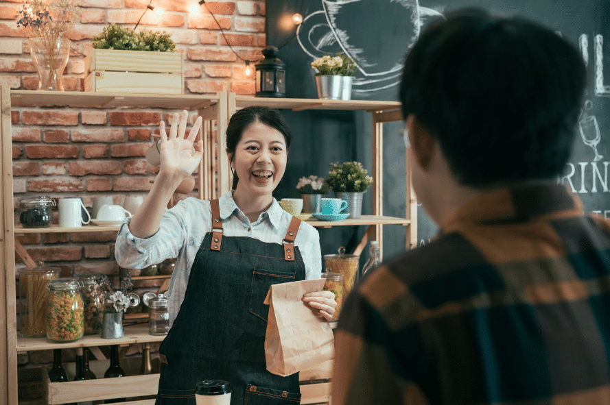 Chinese woman in a shop waving to a customer.